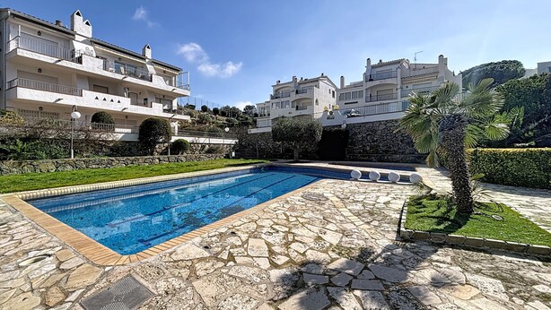 A swimming pool with stone tiles, surrounded by a stone pathway, and adjacent to a building with balconies.