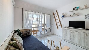 A living room with a sofa, a TV, a small table, and a balcony with a view.