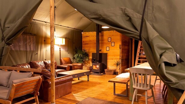 A cozy tented accommodation with a wooden interior, a sofa set, a table, and a fireplace. - Awe Inspiring two Storey Tent (Battle)