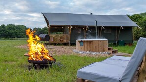 A rustic outdoor setting with a fire pit, a hot tub, and a wooden deck. - Awe Inspiring two Storey Tent (Battle)