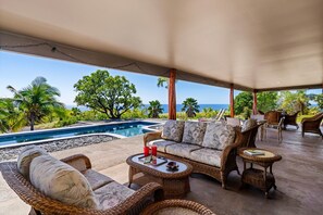 A covered outdoor seating area with wicker furniture, a pool, and a view of the ocean. - Kohala Estate Home 3 Bedroom Estate by RedAwning (Kamuela)