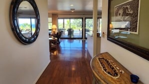 A hallway with wooden flooring, a round mirror, and a wooden console table with decorative items. - Kohala Estate Home 3 Bedroom Estate by RedAwning (Kamuela)