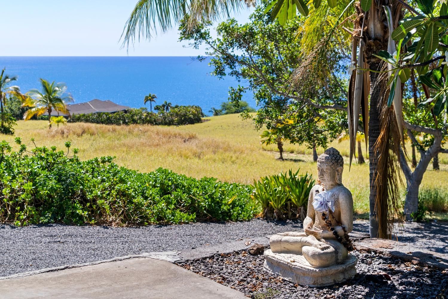 A statue of a seated figure in a garden setting with a view of the ocean.