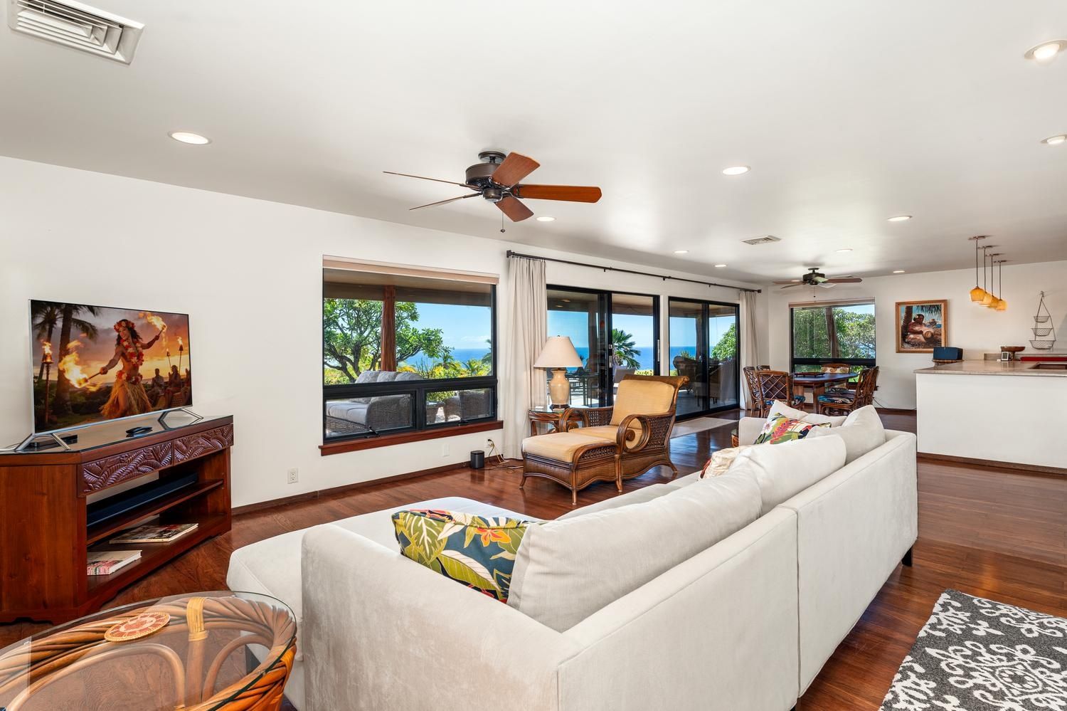 A spacious living room with a large sofa, a television, and a dining area with a view of the ocean.