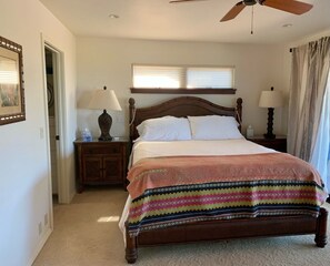 Un dormitorio con una cama de madera, dos mesitas de noche con lámparas, un ventilador de techo y una ventana con persianas.
