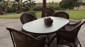 A covered patio with wicker furniture and a table, overlooking a beach and palm trees during sunset. - Kohala Estate Home 3 Bedroom Estate by RedAwning (Kamuela)