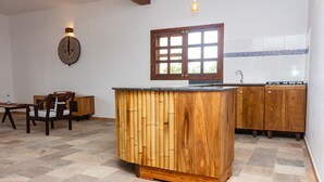 Una cocina con una isla de madera, un comedor con una silla y un ventanal con persianas.
