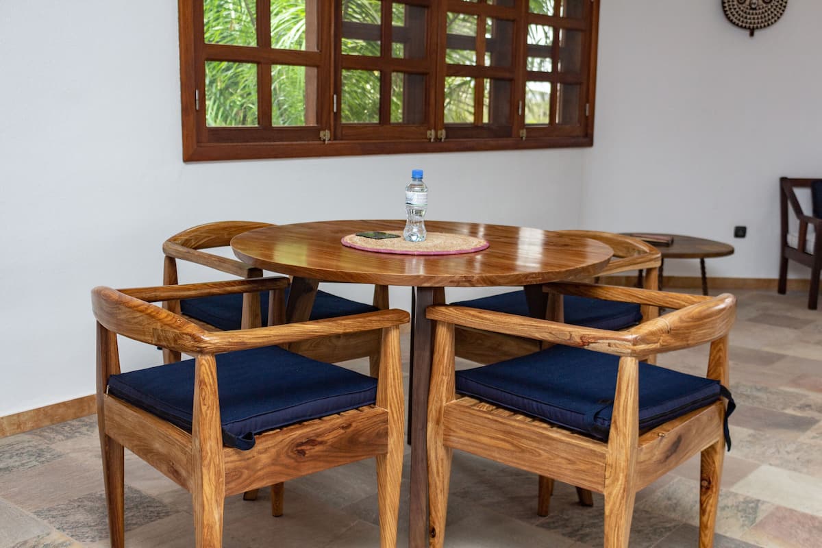 Uma mesa de madeira redonda com uma garrafa de água sobre um jogo americano, rodeada por quatro cadeiras de madeira com almofadas azuis.