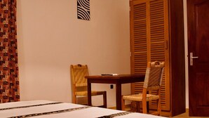 Una habitación de hotel con una cama, dos sillas de madera, una mesita y una puerta de madera.