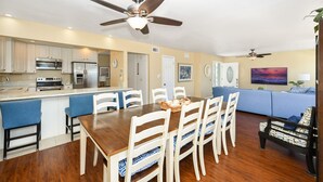 A modern kitchen with stainless steel appliances, a dining area with a wooden table and white chairs, and a living area with a sofa and a ceiling fan. - 4 Bedroom Home Steps to the Sand in Newport Beach (Newport Beach)