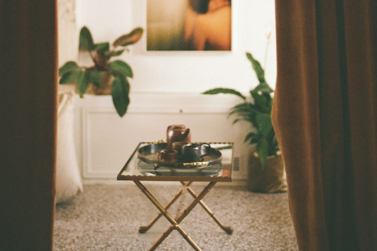 Ein Zimmer mit einem kleinen Tisch, auf dem ein Teekessel und Tassen stehen, einer Topfpflanze und einem Bild an der Wand.