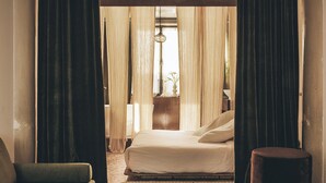 A bedroom with a bed, a bedside table with a lamp, and a window with curtains. - Mona Athens. (Athens)