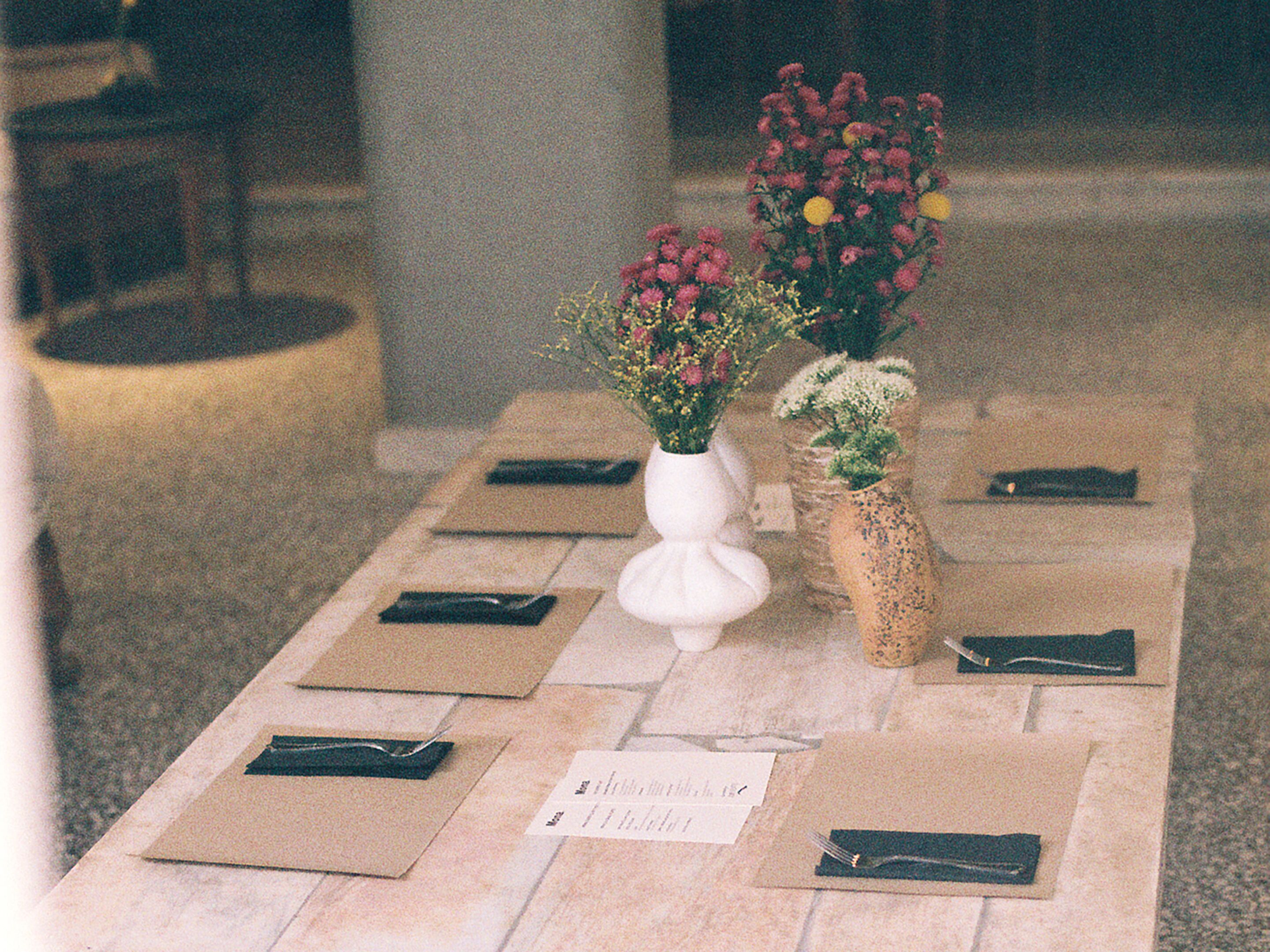Een tafel met bloemen in vazen en opgevouwen servetten op een betegelde vloer.