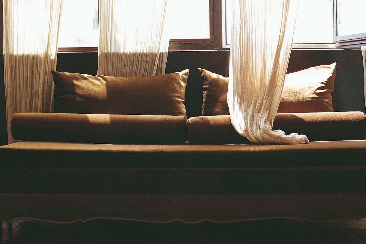 Ein Sofa mit Kissen und durchsichtigen Vorhängen in einem Raum.
