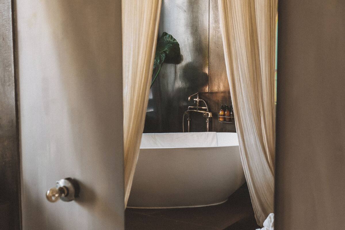 Ein Schlafzimmer mit einem Bett, Kissen, einem Nachttisch, einem Spiegel und einem Fenster mit Vorhängen.