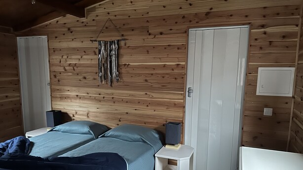 Una habitación acogedora con paredes de madera, una cama con ropa de cama azul, una mesita de noche con una lámpara y un armario.