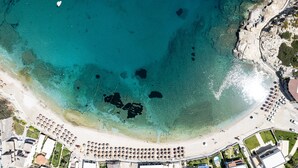 Vista aérea de una playa con agua turquesa cristalina, una orilla arenosa y una hilera de sombrillas.