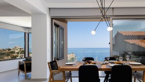 Un comedor con vistas al mar, una mesa lista para dos personas y una silla con cojín.