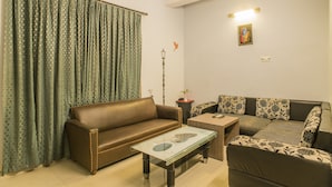 A living room with a brown sofa, a glass coffee table, and a patterned sofa. - Utsav Resort by The Citi Residenci (Durgapur)
