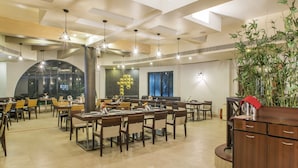 A spacious dining area with multiple tables and chairs, a large plant, and a modern ceiling design. - Utsav Resort by The Citi Residenci (Durgapur)