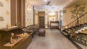 A hotel lobby with a reception desk, seating area, staircase, and decorative wall art. - Utsav Resort by The Citi Residenci (Durgapur)