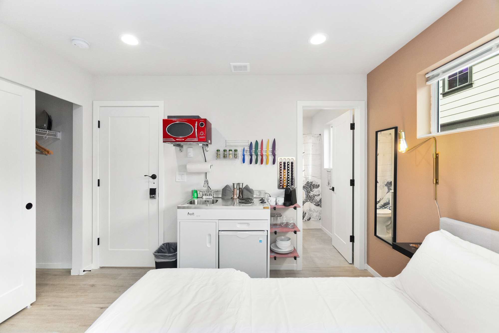 Une chambre d’hôtel moderne équipée d’un lit, d’une kitchenette, d’une salle de bain et d’un grand miroir.