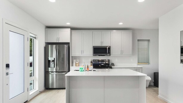 A modern kitchen with a central island, stainless steel appliances, and white cabinetry. - Chase's sweet suite - Micro Studio - 91Walkscore (Seattle)