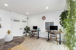 Una habitación moderna con dos escritorios, sillas, una puerta blanca y un televisor montado en la pared.