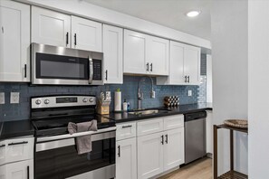 A modern kitchen with white cabinets, a stainless steel microwave, a gas stove, and a dishwasher. - Stylish 2 bedroom apartment poolside OT-Scottsdale (Scottsdale)