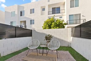 Ein kleiner Patio-Bereich mit zwei weißen Stühlen und einem Tisch, umgeben von einer niedrigen Ziegelmauer und einem Metallzaun.