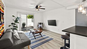 A modern living room with a grey sofa, a coffee table, a TV mounted on the wall, and a ceiling fan.