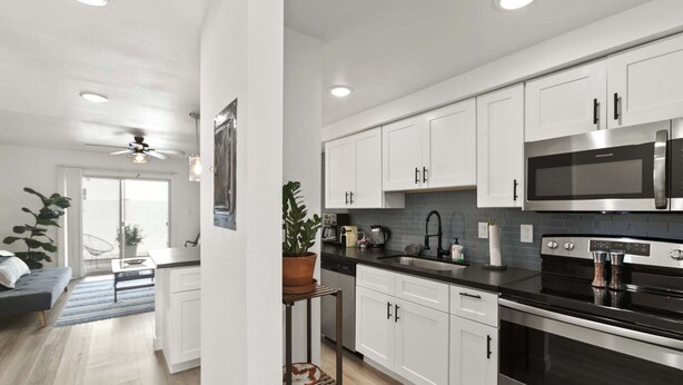 A modern kitchen with white cabinets, stainless steel appliances, and a black countertop.