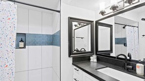 A modern bathroom with a shower, a large mirror, a sink, and a bottle of shampoo.