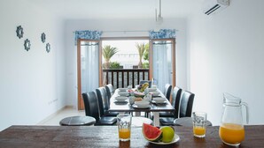 A dining area with a long table set for six, a view of the outdoors, and a balcony with a railing. - 6 Bed Holiday Villa | Heated Pool | Hot Tub | Beach & Waterparks | Playa Blanca (Playa Blanca)