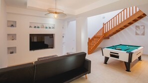 A living room with a pool table, a sofa, a TV mounted on the wall, and a staircase. - 6 Bed Holiday Villa | Heated Pool | Hot Tub | Beach & Waterparks | Playa Blanca (Playa Blanca)