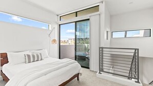 Een moderne slaapkamer met een groot bed, een balkon en uitzicht, en een metalen hekwerk.
