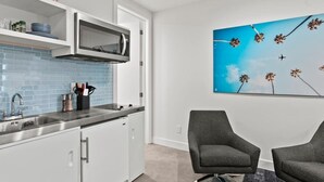 Une cuisine moderne équipée d’un four à micro-ondes, d’un évier et de placards. Un tableau représentant un ciel bleu parsemé de fleurs est accroché au mur.
