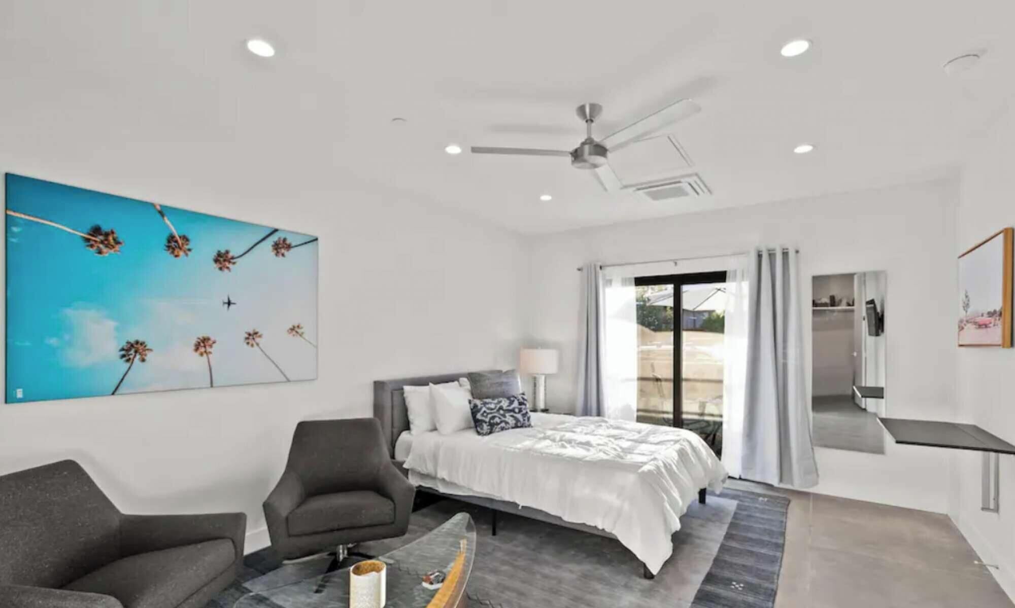 A modern bedroom with a bed, a desk, a chair, and a ceiling fan.