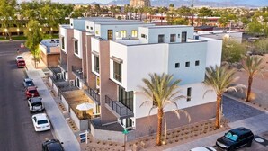 Un immeuble moderne à plusieurs étages, doté d’un toit plat, d’un parking et de palmiers.