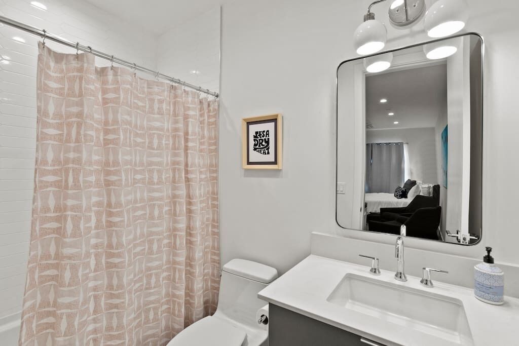 A modern bathroom with a shower curtain, toilet, sink, and mirror.