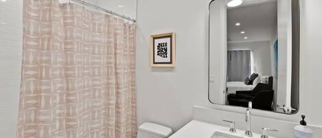 A modern bathroom with a shower curtain, toilet, sink, and mirror.
