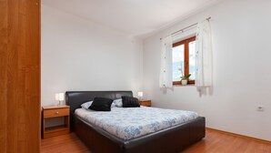 Ein Schlafzimmer mit einem Bett, Nachttischen aus Holz, einem Fenster mit Vorhängen und einer Topfpflanze.