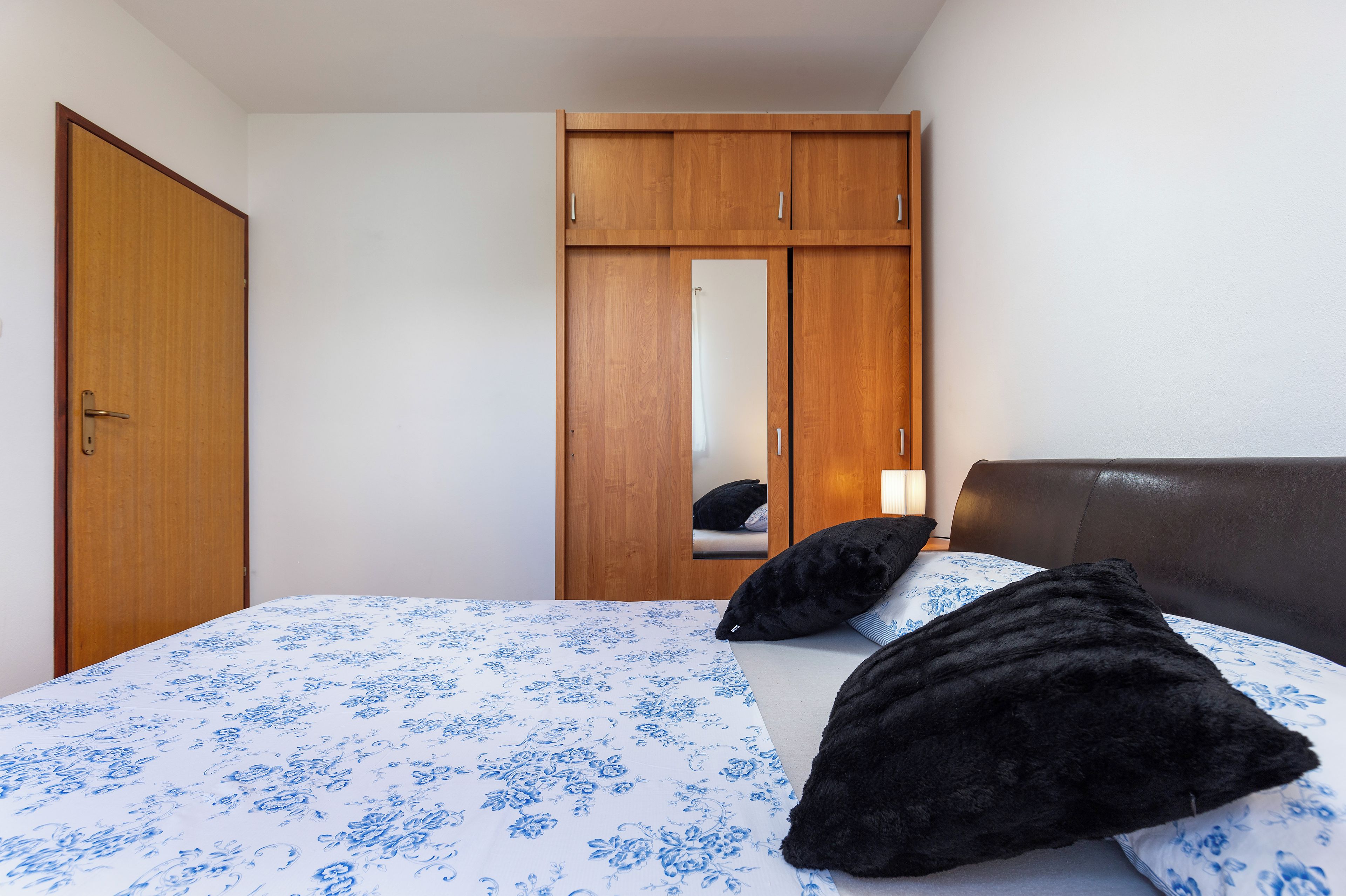 A bedroom with a bed, a wooden wardrobe, and a mirror.