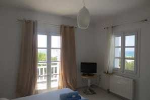 A room with a bed, a television on a stand, and large windows with curtains.