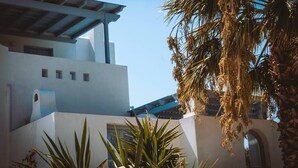 A modern building with a flat roof and white walls, surrounded by palm trees and other greenery. - Riviera paradise villa with private pool (Amorgos)