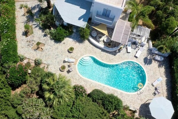 An aerial view of a property with a swimming pool surrounded by lounge chairs and a small deck area.