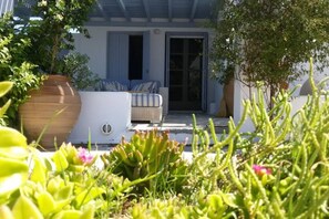 A covered outdoor seating area with a sofa and chairs, surrounded by potted plants and a small garden.