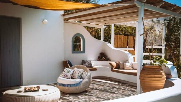 A sunlit outdoor seating area with a round wicker sofa, a cushioned bench, and a large terracotta pot. - Riviera paradise villa with private pool (Amorgos)