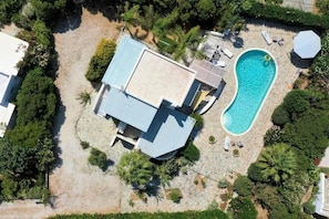 An aerial view of a property with a swimming pool, a covered patio, and surrounding greenery.