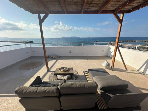 A rooftop terrace with a view of the sea, a covered seating area, and a table with a vase.